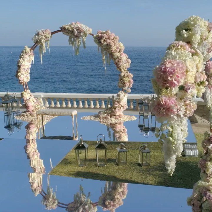 Circular floral arch and mirrored floor overlooking the ocean for a wedding ceremony.