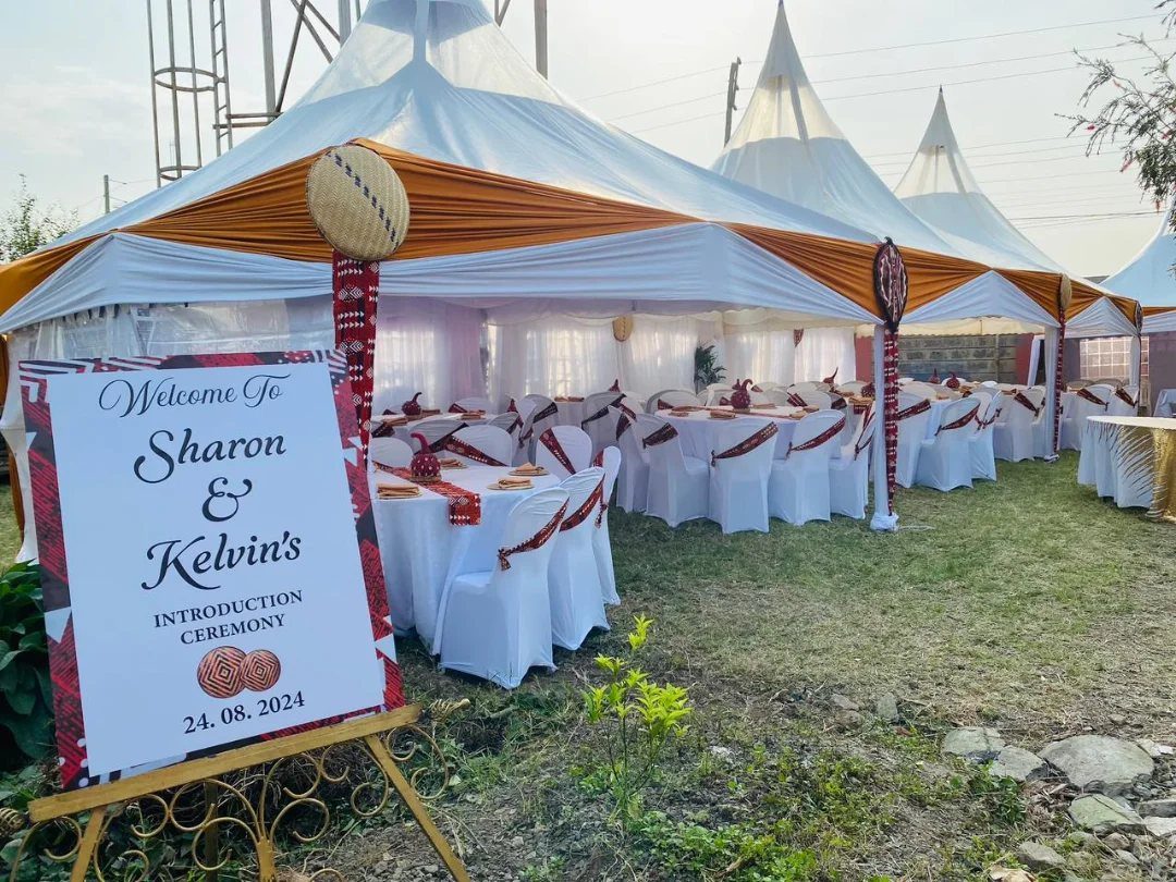 Outdoor ceremony setup with white peaked tents, decorated tables, and a welcome sign.