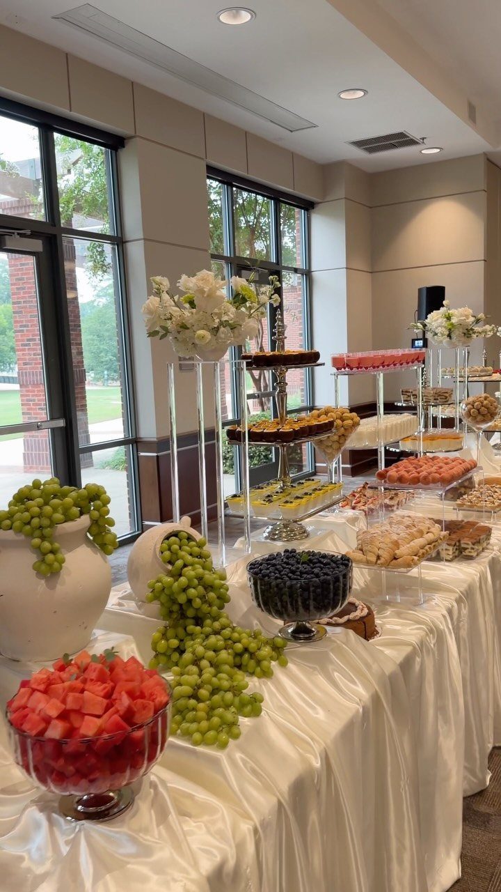 Dessert buffet table with fresh fruit, tiered cakes, and white floral centerpieces.