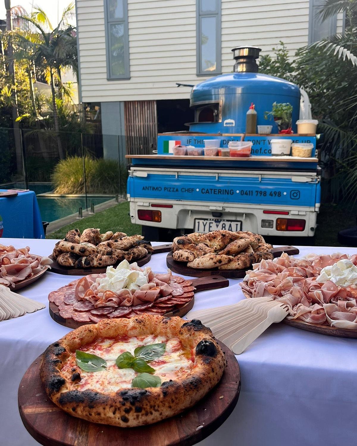 Margherita pizza and charcuterie boards on a table with a blue pizza truck.