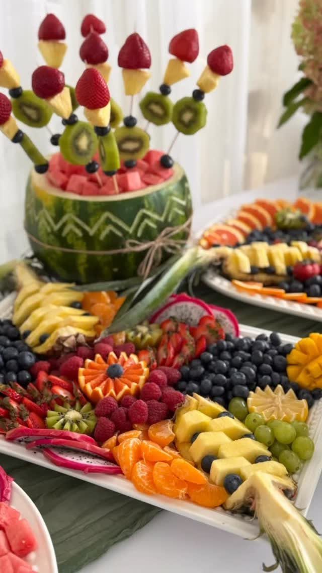 Fresh fruit platters with carved watermelon skewers, blueberries, raspberries, and sliced pineapple.