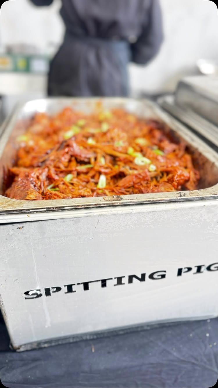 Pulled pork in a metal catering tray labeled Spitting Pig with green onion garnish.
