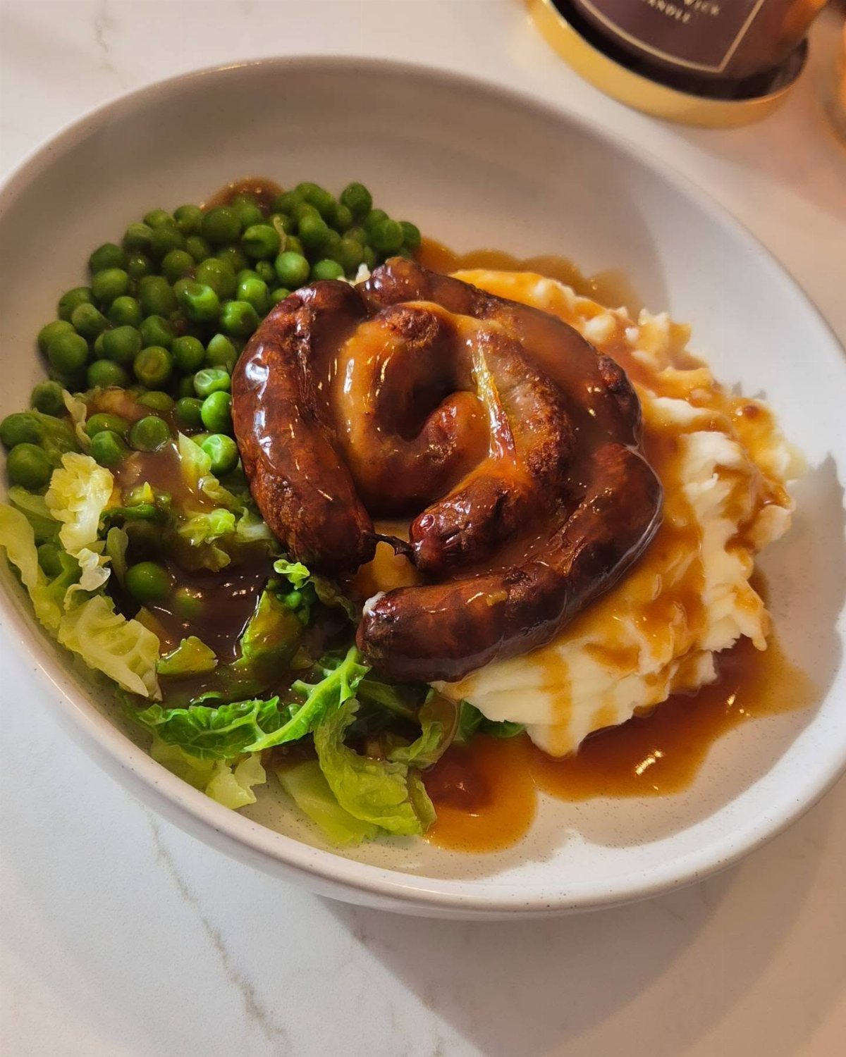 Coiled sausages with brown gravy on mashed potatoes with peas and cabbage.