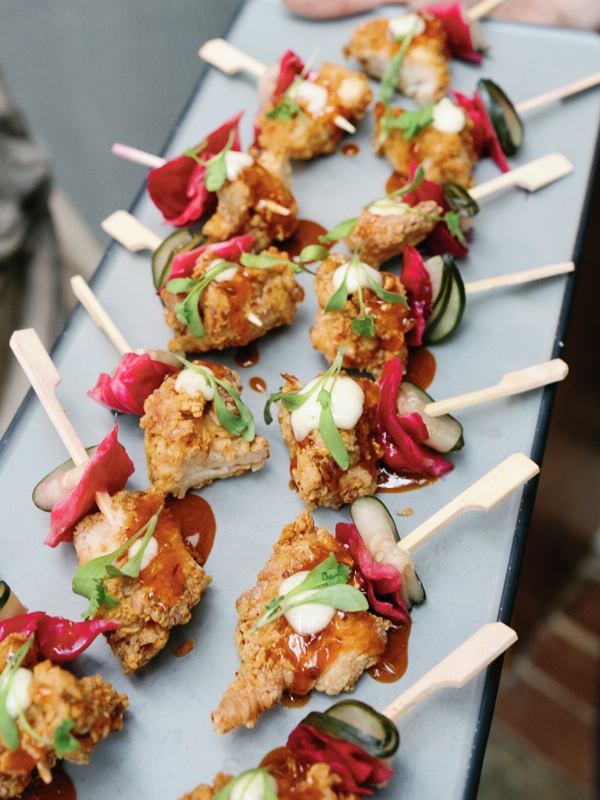Fried chicken skewers with pickled onions and sauce on a grey platter