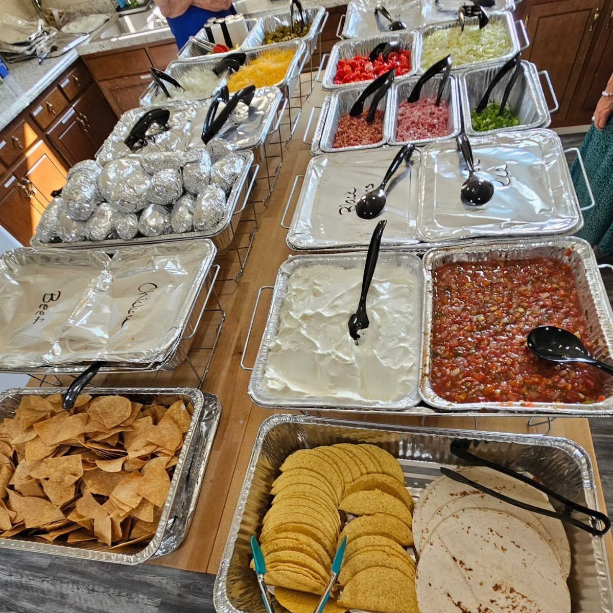 Baked potato and taco bar with foil-wrapped potatoes, chips, shells, and toppings.