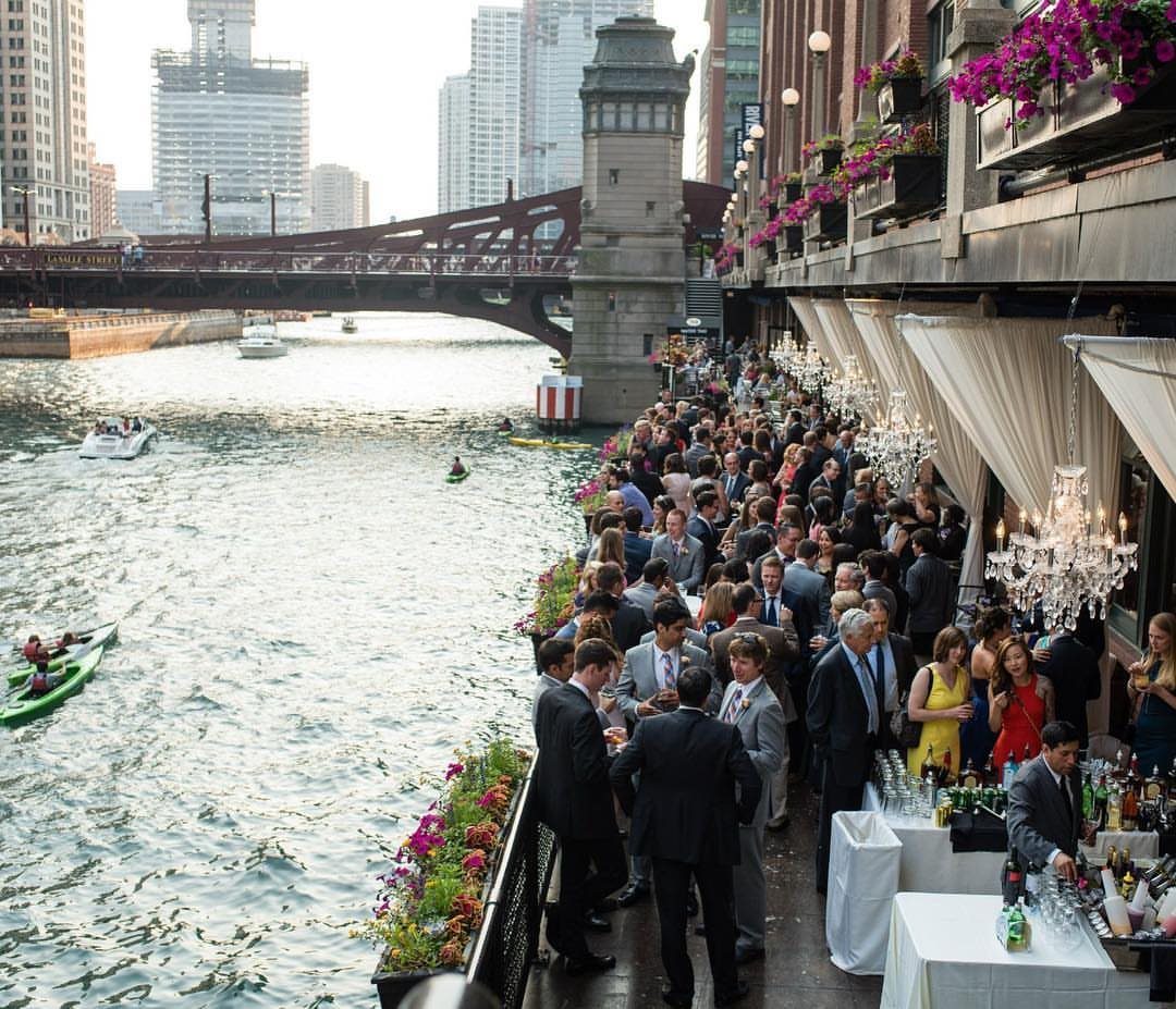 Formal guests gathering on a riverside terrace overlooking the Chicago River and skyline.