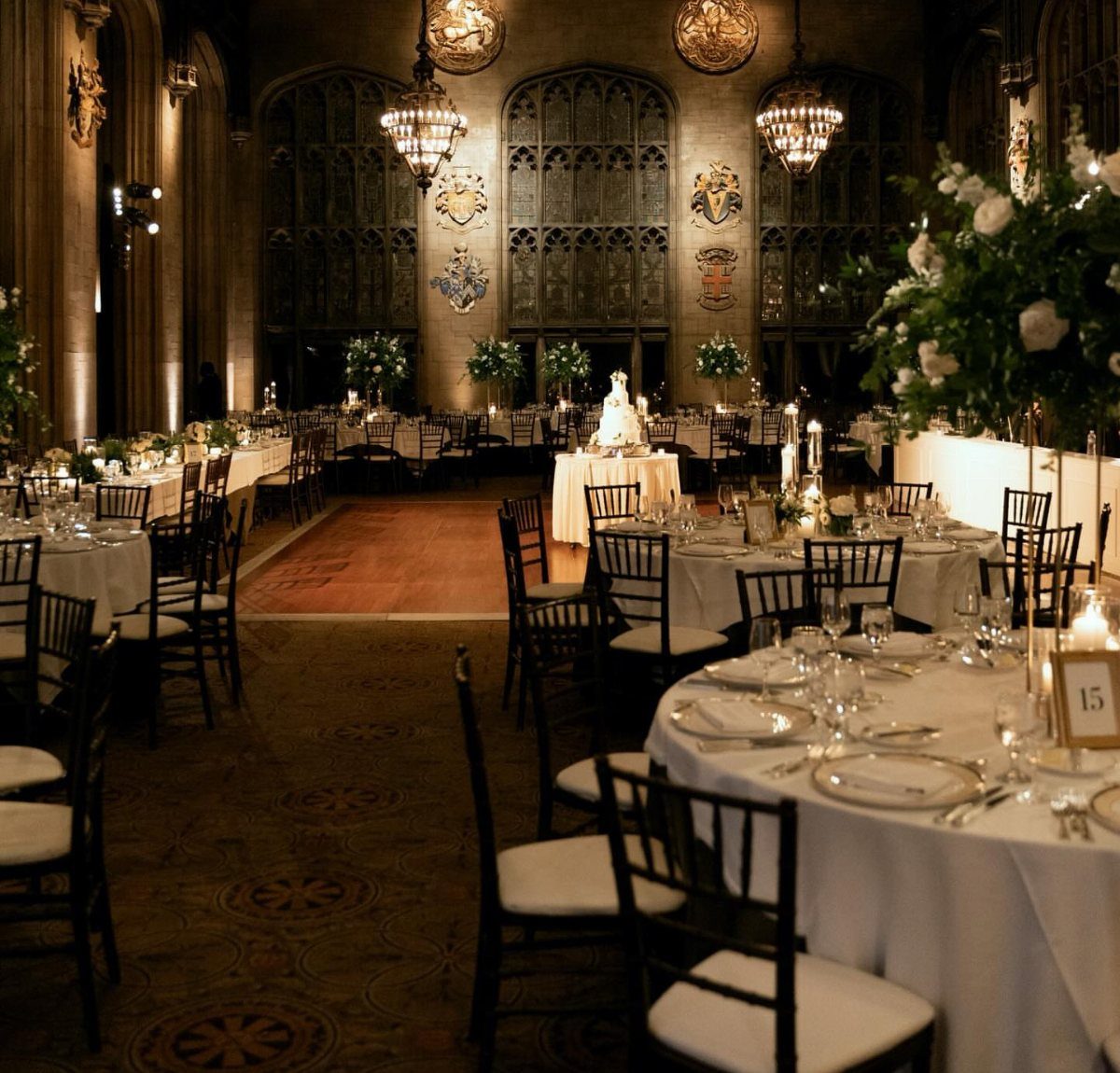 Grand historic hall with round wedding tables, white linens, and ornate chandeliers.
