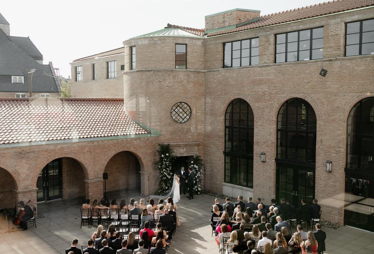 Wedding ceremony in a brick courtyard with guests seated before a couple.