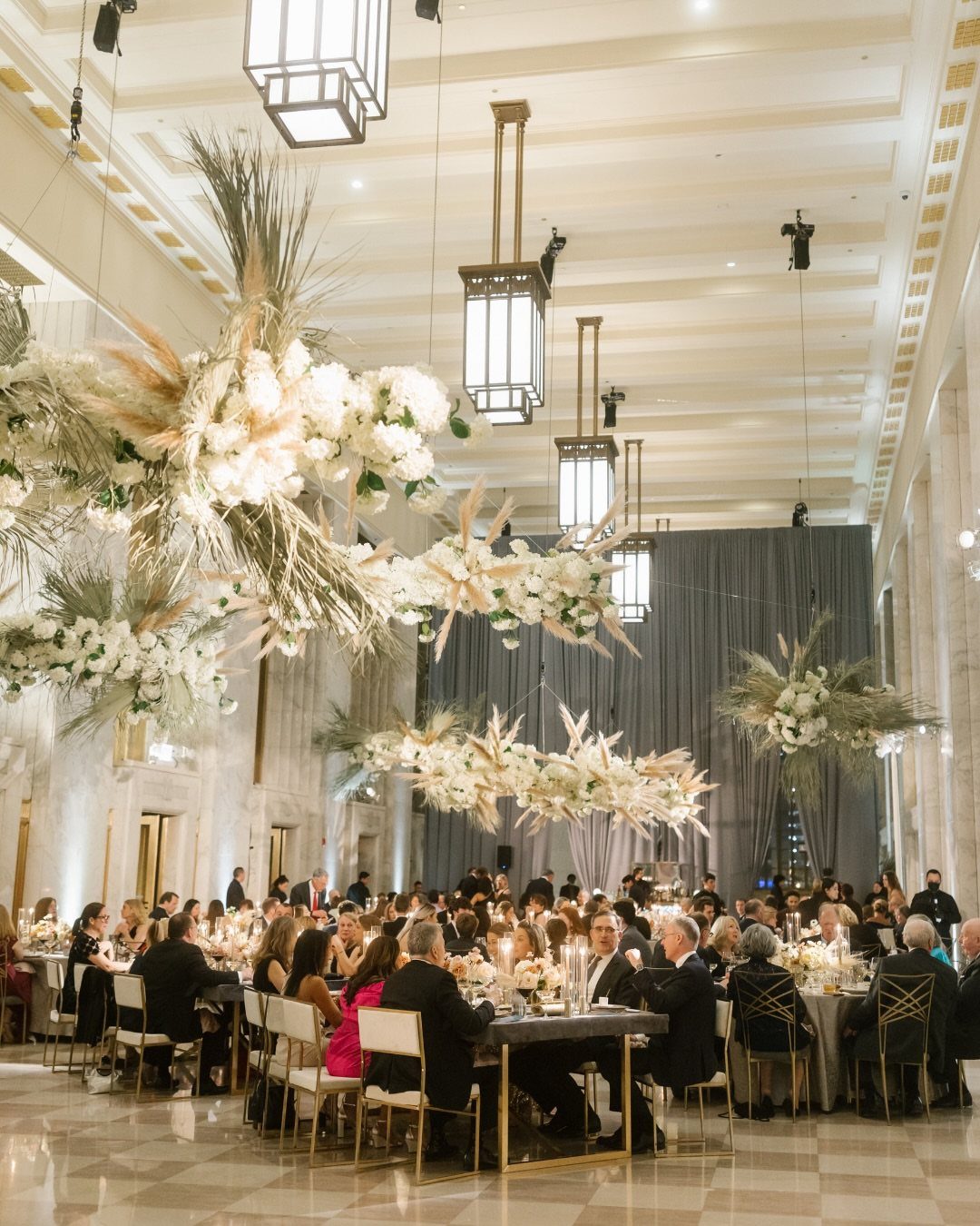 Wedding reception in a grand hall with white marble walls and floral installations.