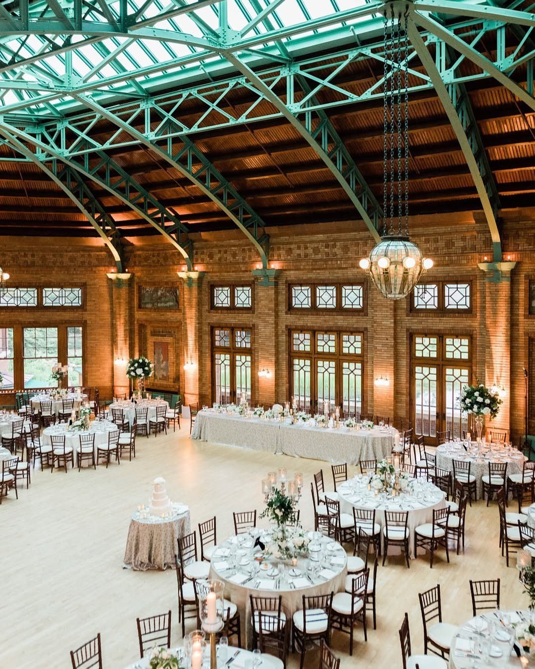 Wedding reception setup with teal steel ceiling trusses and white linen tables