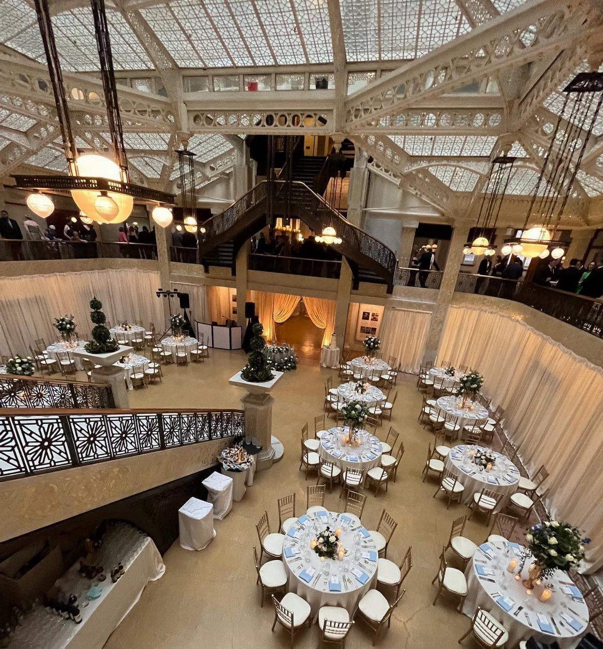 Grand indoor venue with glass ceiling, ornate staircase, and set wedding tables.