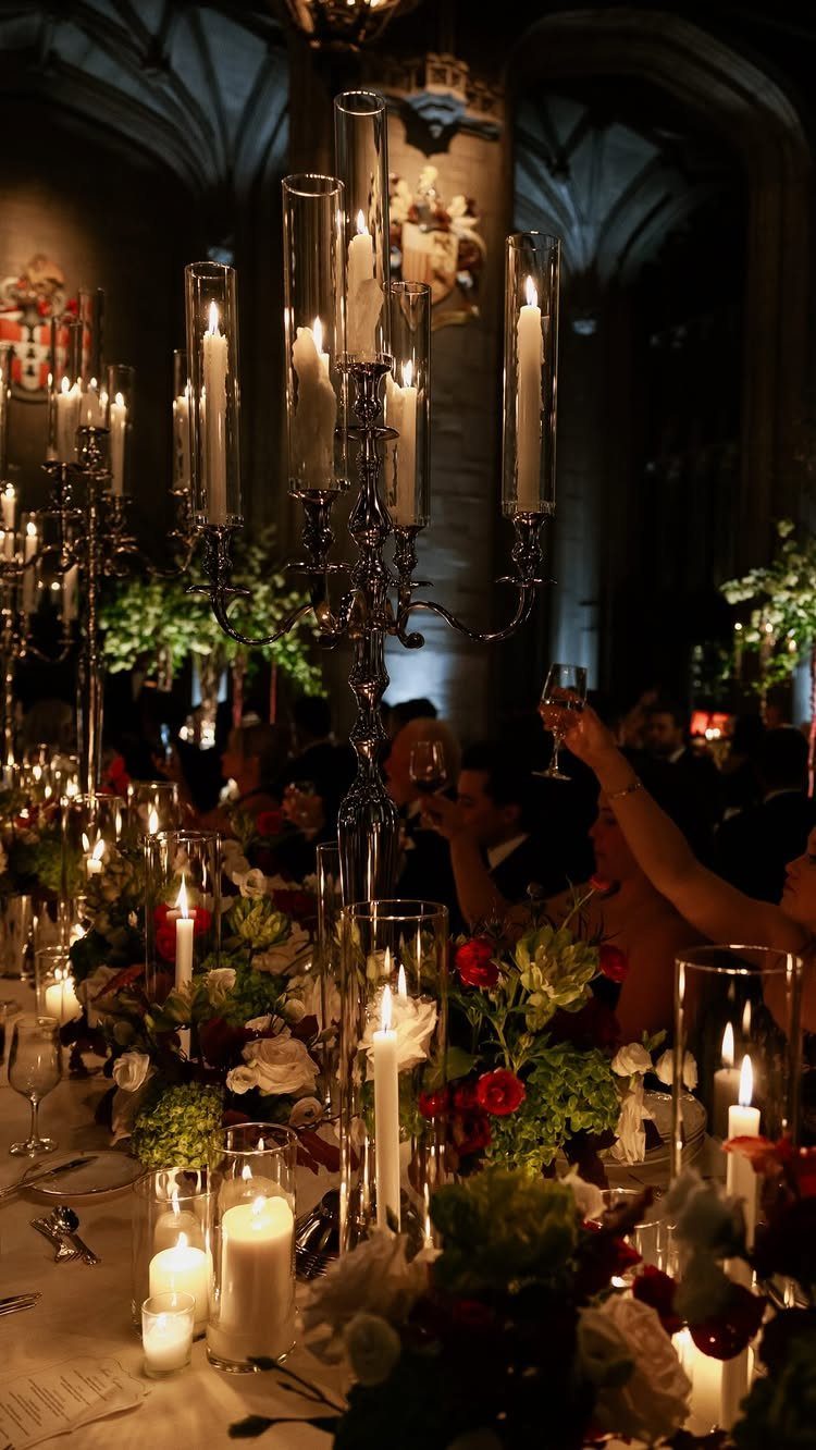 Elegant wedding table setting with tall candles, red flowers, and gothic architecture.