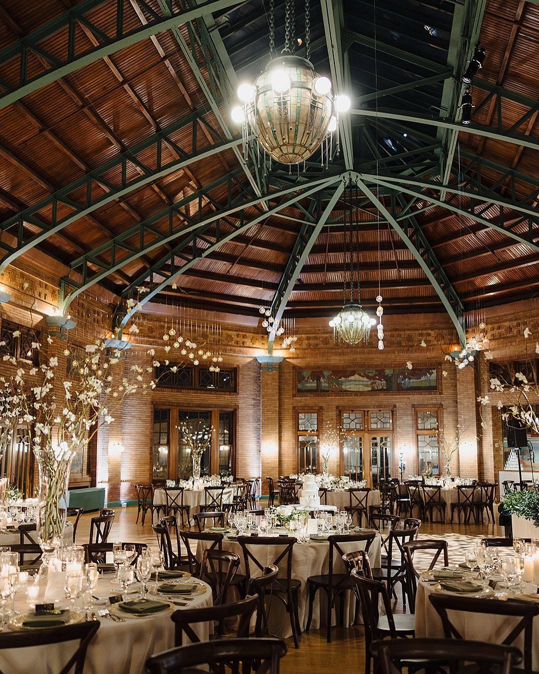 Wedding reception tables under a vaulted wooden ceiling with green metal trusses
