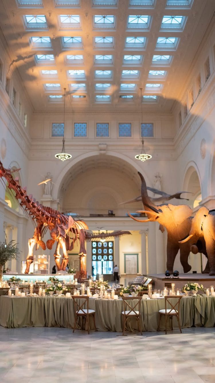 Dinosaur skeletons standing beside a long, decorated wedding banquet table in a grand hall.