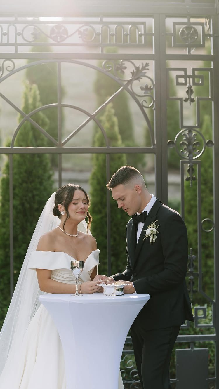 Bride and groom taking communion at a small white table during their wedding ceremony.