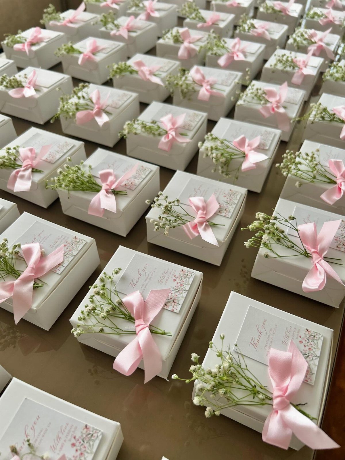 Small white gift boxes with pink ribbons and baby's breath flowers on a table.