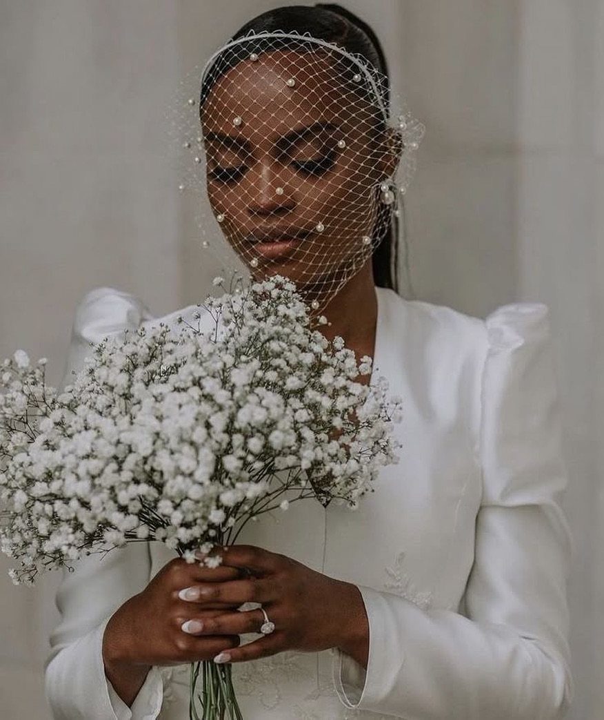 Woman in white bridal attire wearing a pearl birdcage veil holding baby's breath.
