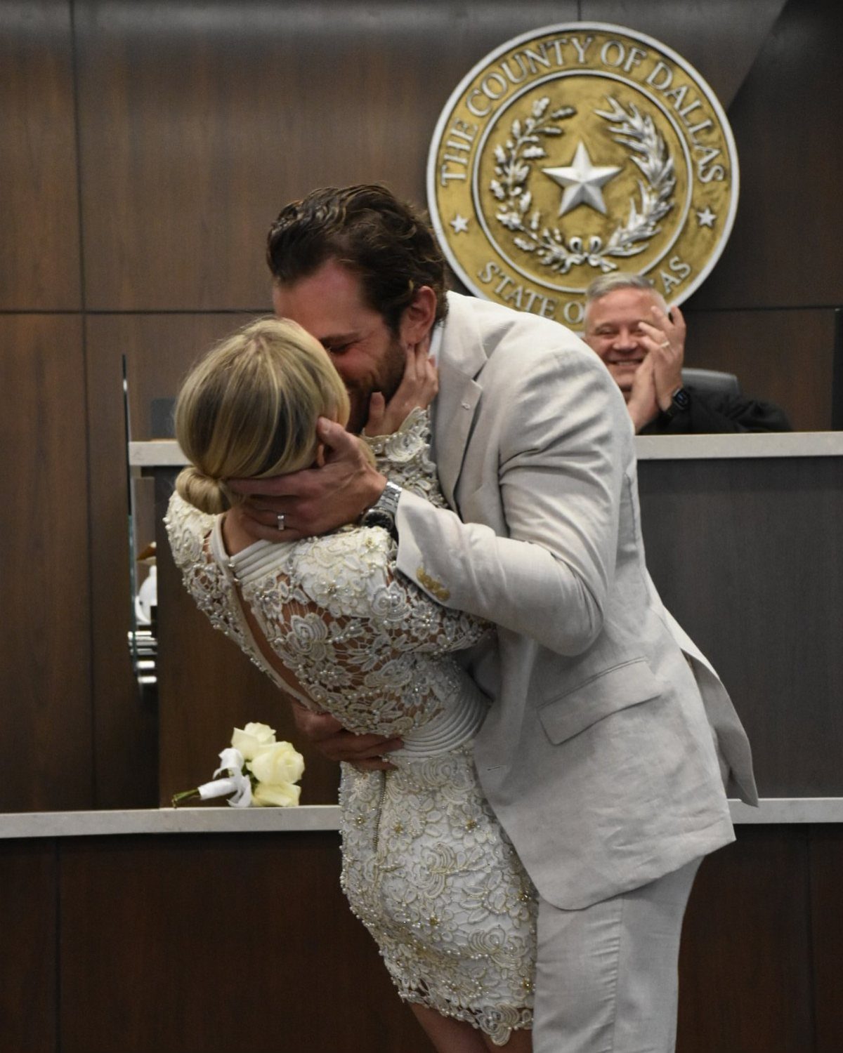 Couple hugging at a courthouse wedding, woman wearing a beaded white lace dress.