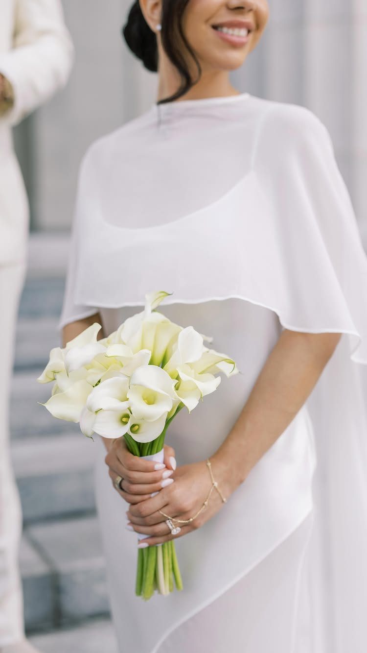 Woman in a white bridal gown with a cape holding calla lilies