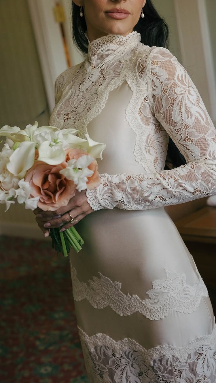 Woman in a cream lace wedding dress holding a white and peach bouquet.