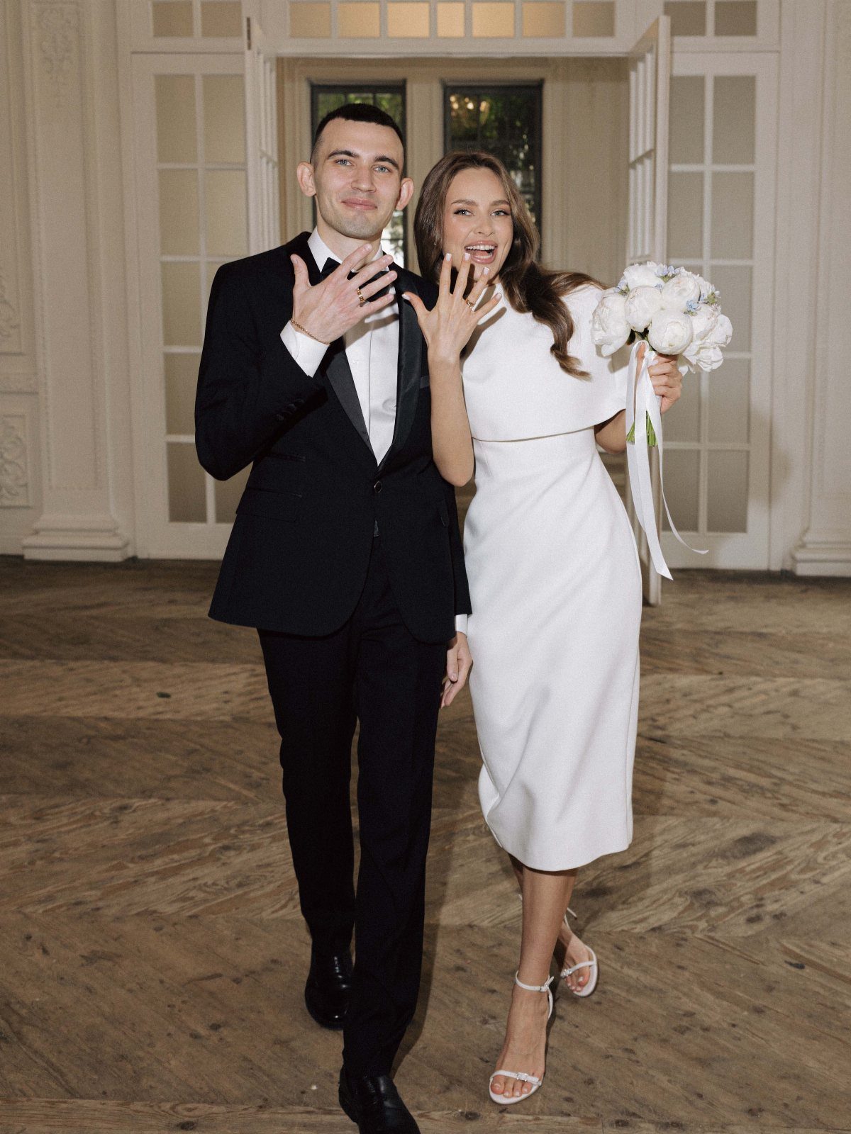 Couple in wedding attire, man in tuxedo and woman in white midi dress.
