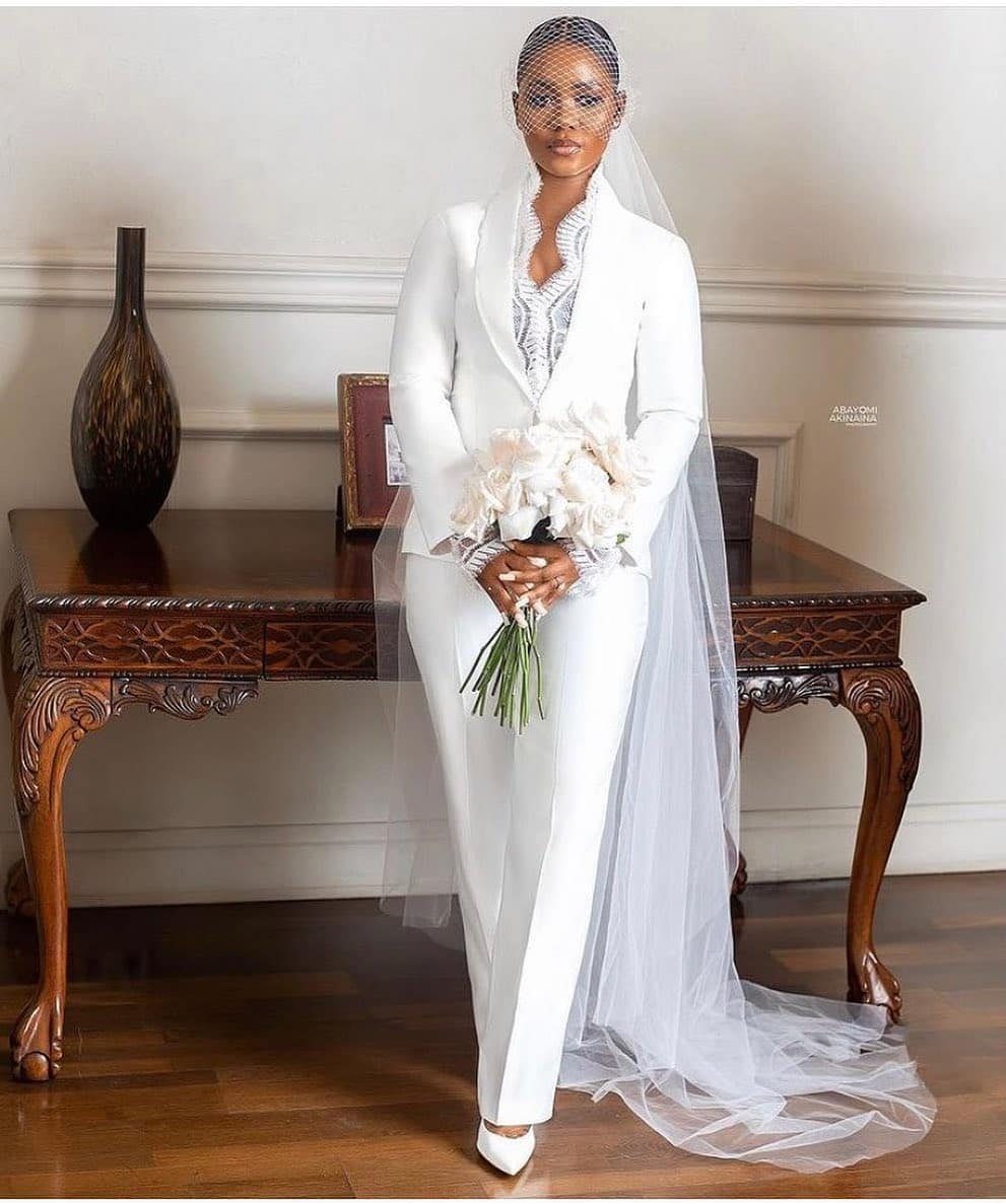 Woman in a white tailored bridal jumpsuit with a veil holding white flowers.