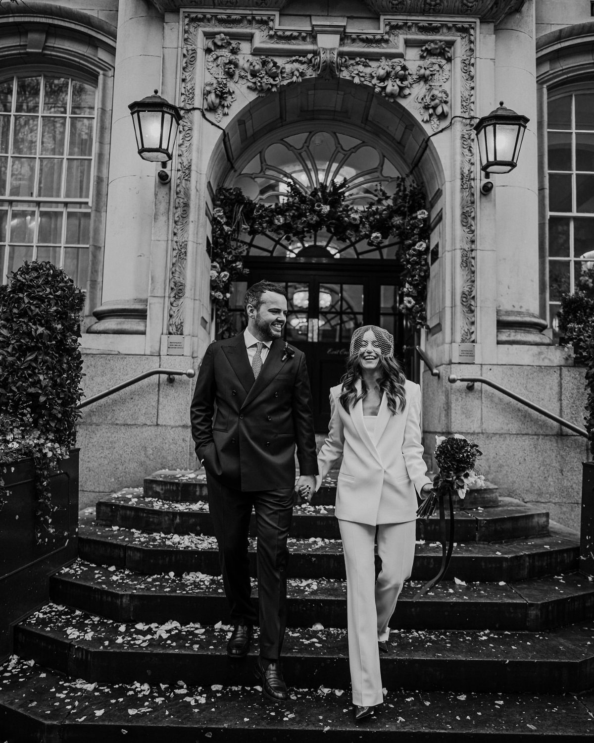 Couple walking down steps, woman wearing a white blazer and wide-leg pants.