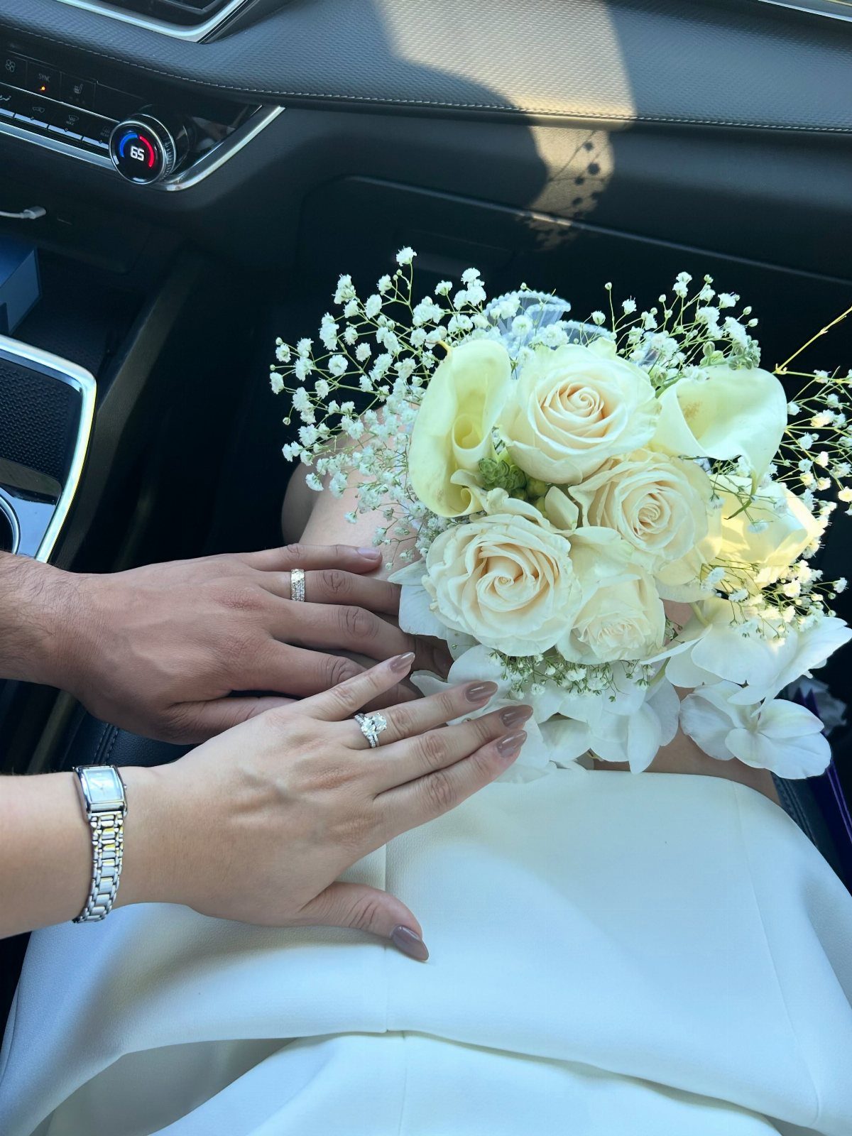 Wedding bouquet of white roses and baby's breath held by a couple's hands.