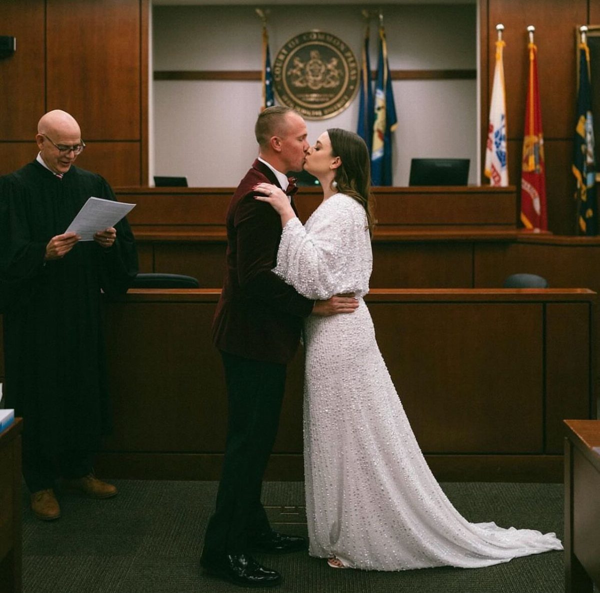 Couple kissing in a courtroom during a wedding ceremony with a judge present