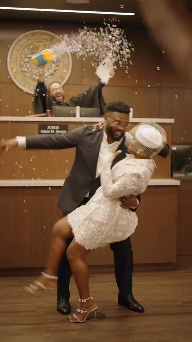 Couple embracing in a dip while a judge throws confetti in a courtroom.