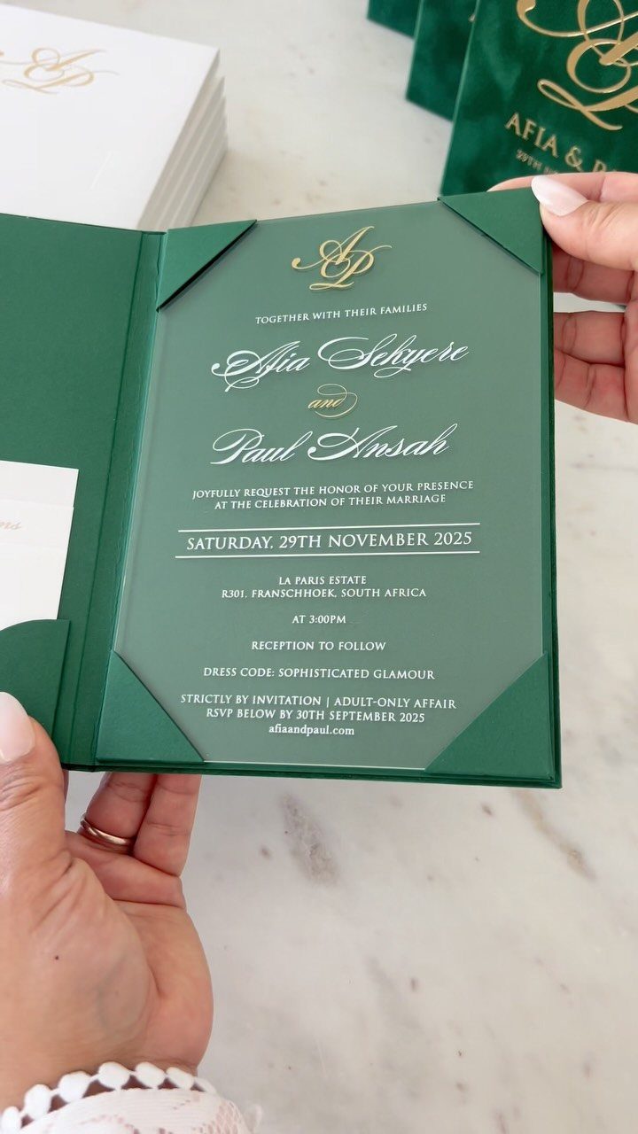 Green wedding invitation with gold foil lettering held by two hands.
