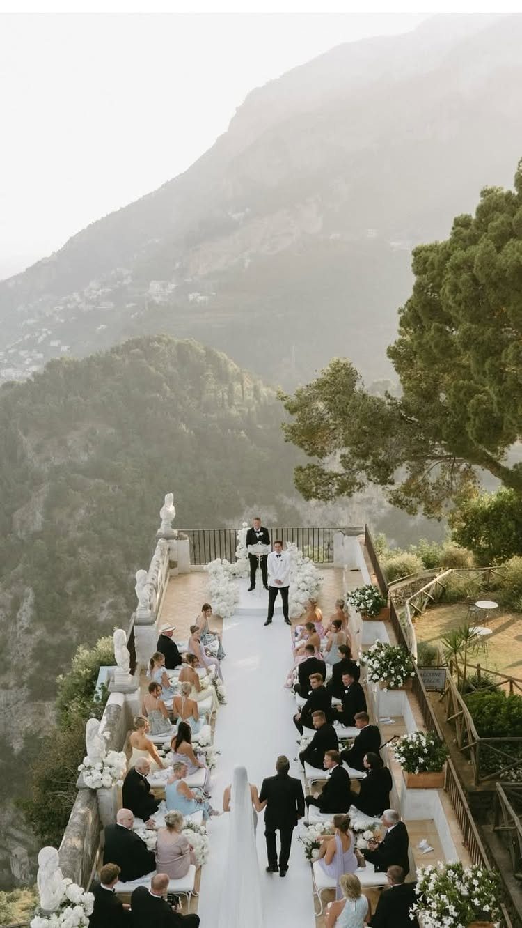 Wedding ceremony on a cliffside terrace with white flowers overlooking Italian mountains