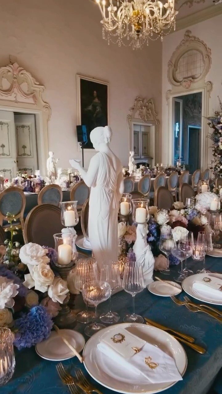 Ornate ballroom table setting with blue linens, white flowers, and a classical statue centerpiece.