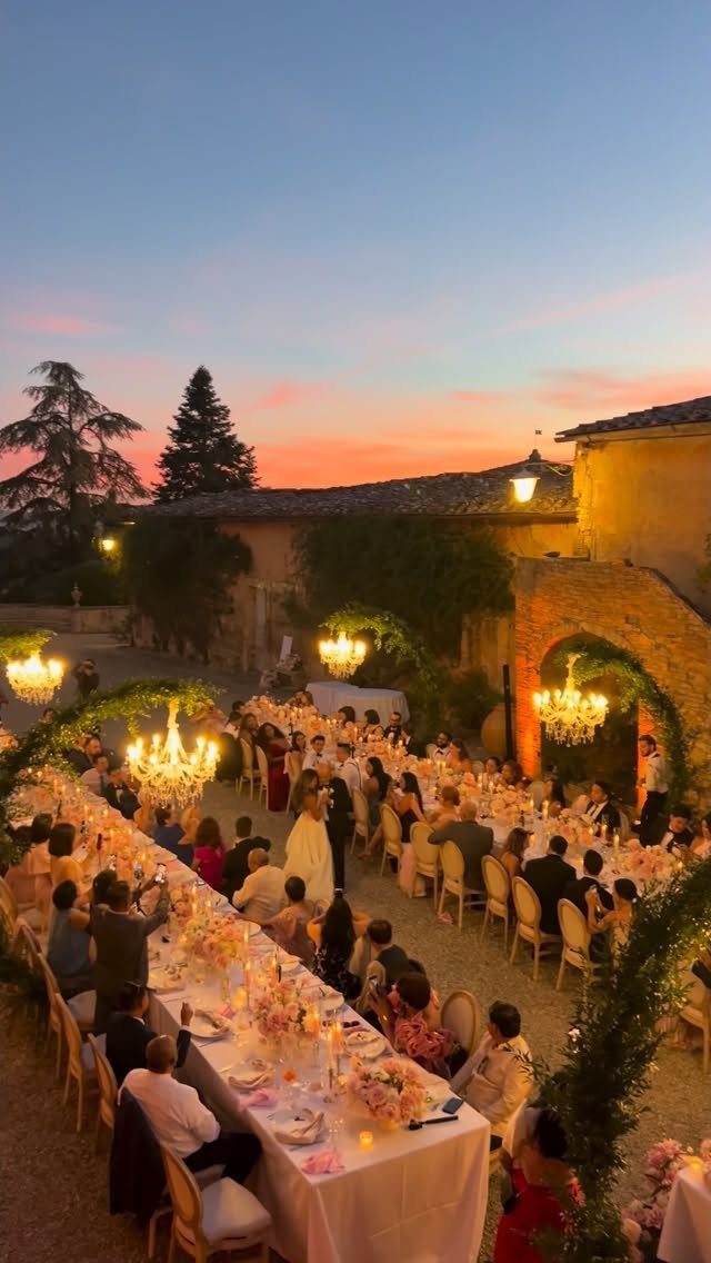 Outdoor wedding banquet at a rustic Italian villa courtyard during a golden sunset.