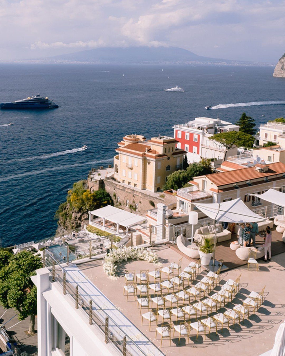 Wedding ceremony setup with gold chairs and floral arch overlooking a coastal town.