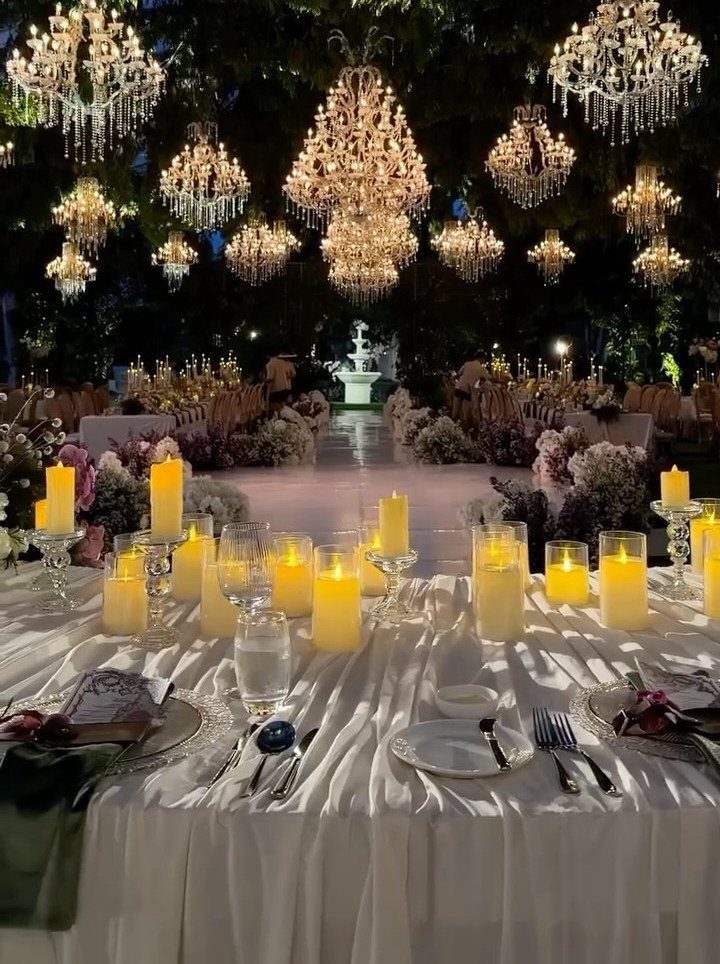 Elegant outdoor wedding reception with glowing candles and crystal chandeliers hanging from trees