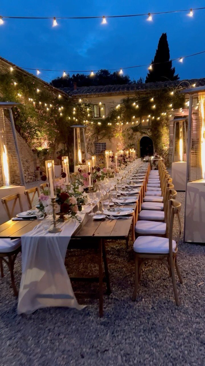 Long wooden wedding table with candles and flowers under string lights at a villa.