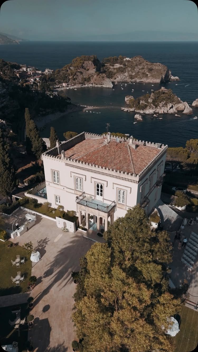 White coastal villa with terracotta roof overlooking the blue sea and rocky islands.