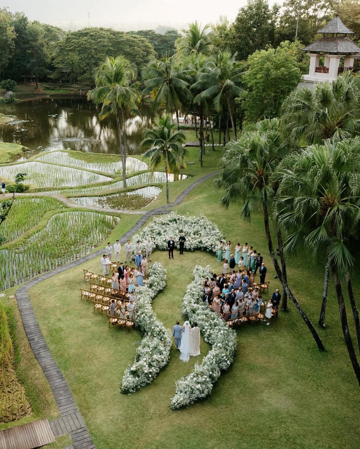 Outdoor wedding ceremony with floral arrangements set amidst tropical palm trees and rice terraces.