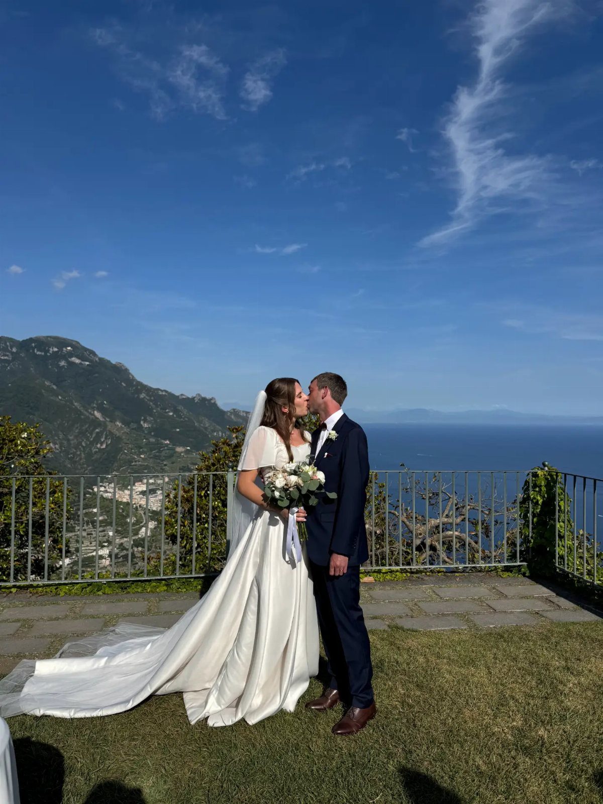 Bride and groom standing on a cliffside terrace overlooking the Amalfi Coast sea.