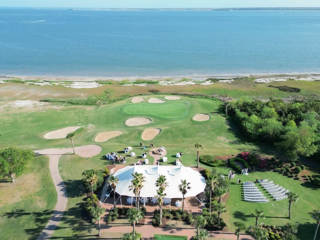 White event tent and wedding seating on a lawn by the ocean coast.