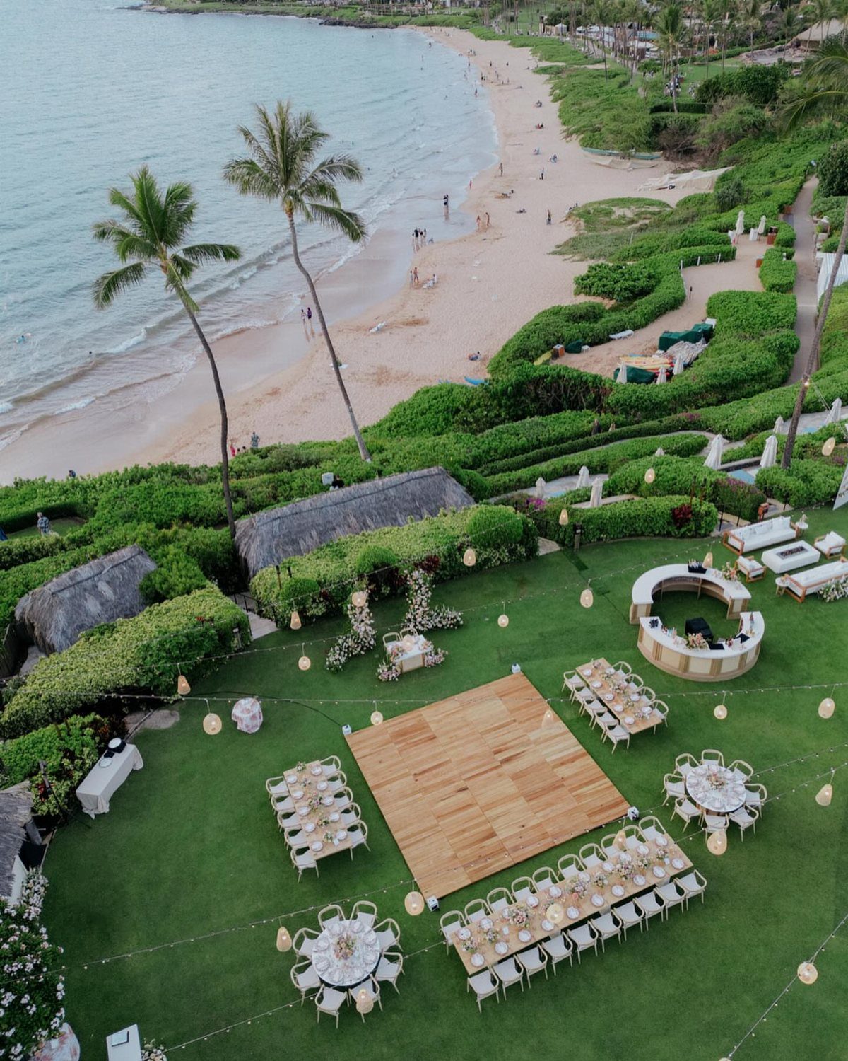 Outdoor wedding reception setup on a green lawn overlooking a tropical sandy beach.