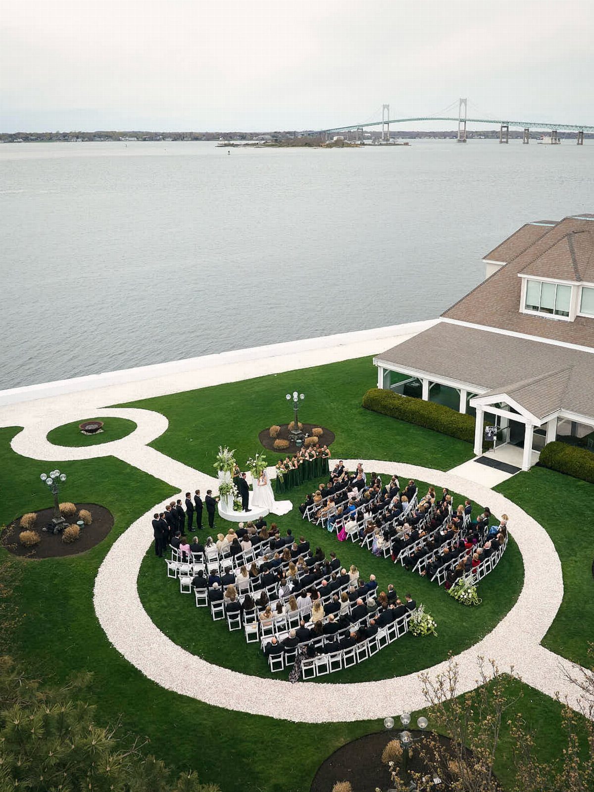 Outdoor wedding ceremony on a green lawn beside a white estate and ocean.