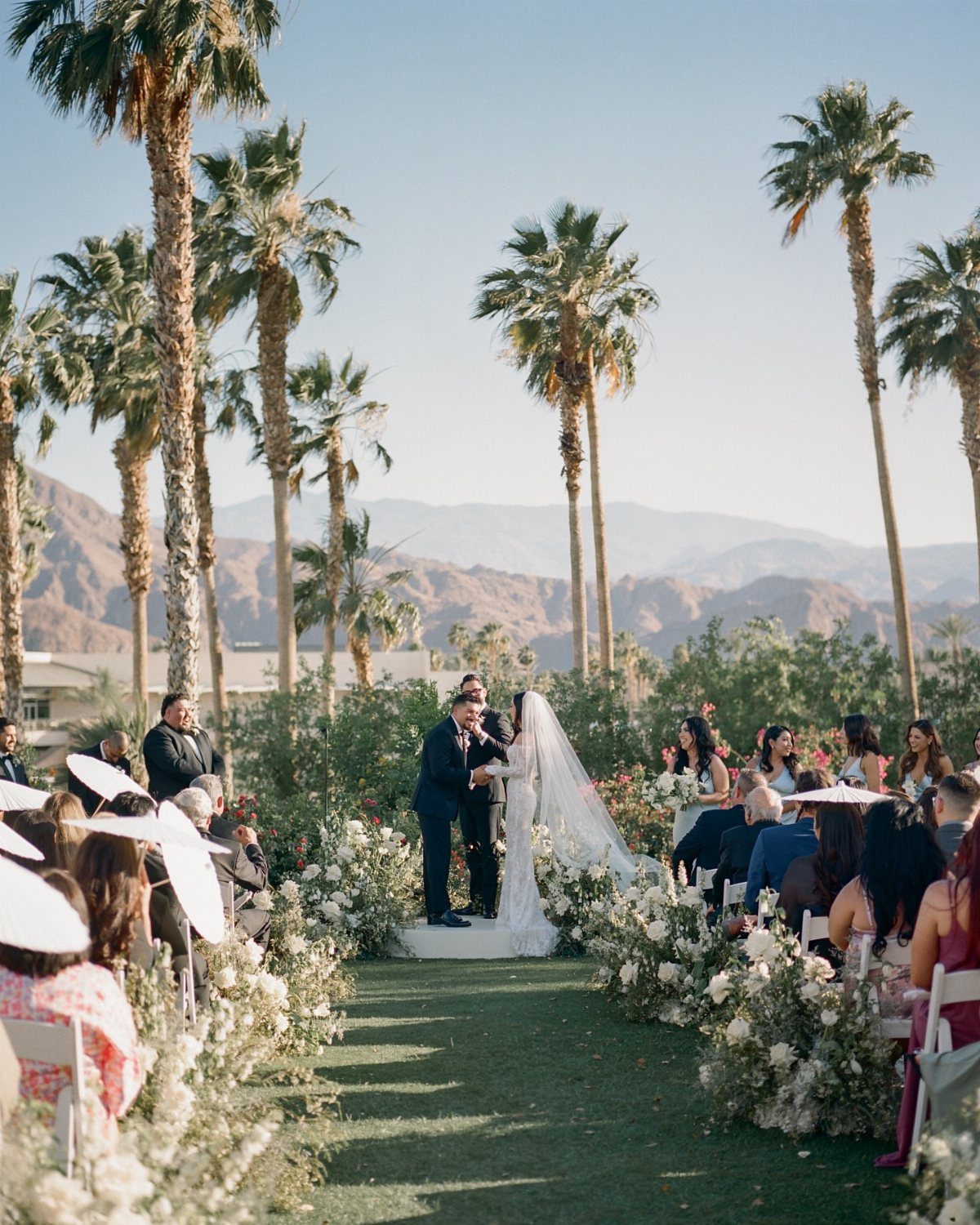 Wedding ceremony in a desert setting with palm trees and distant mountains.