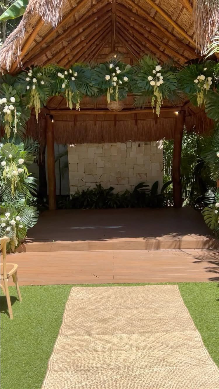 Tropical wedding altar with thatched roof, white flowers, and a tan aisle runner.