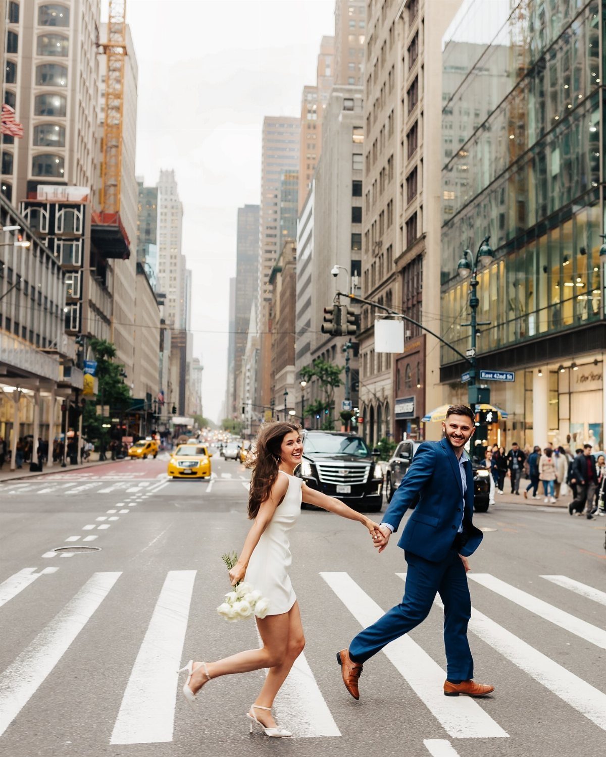 Newlywed couple holding hands while crossing a busy New York City street.