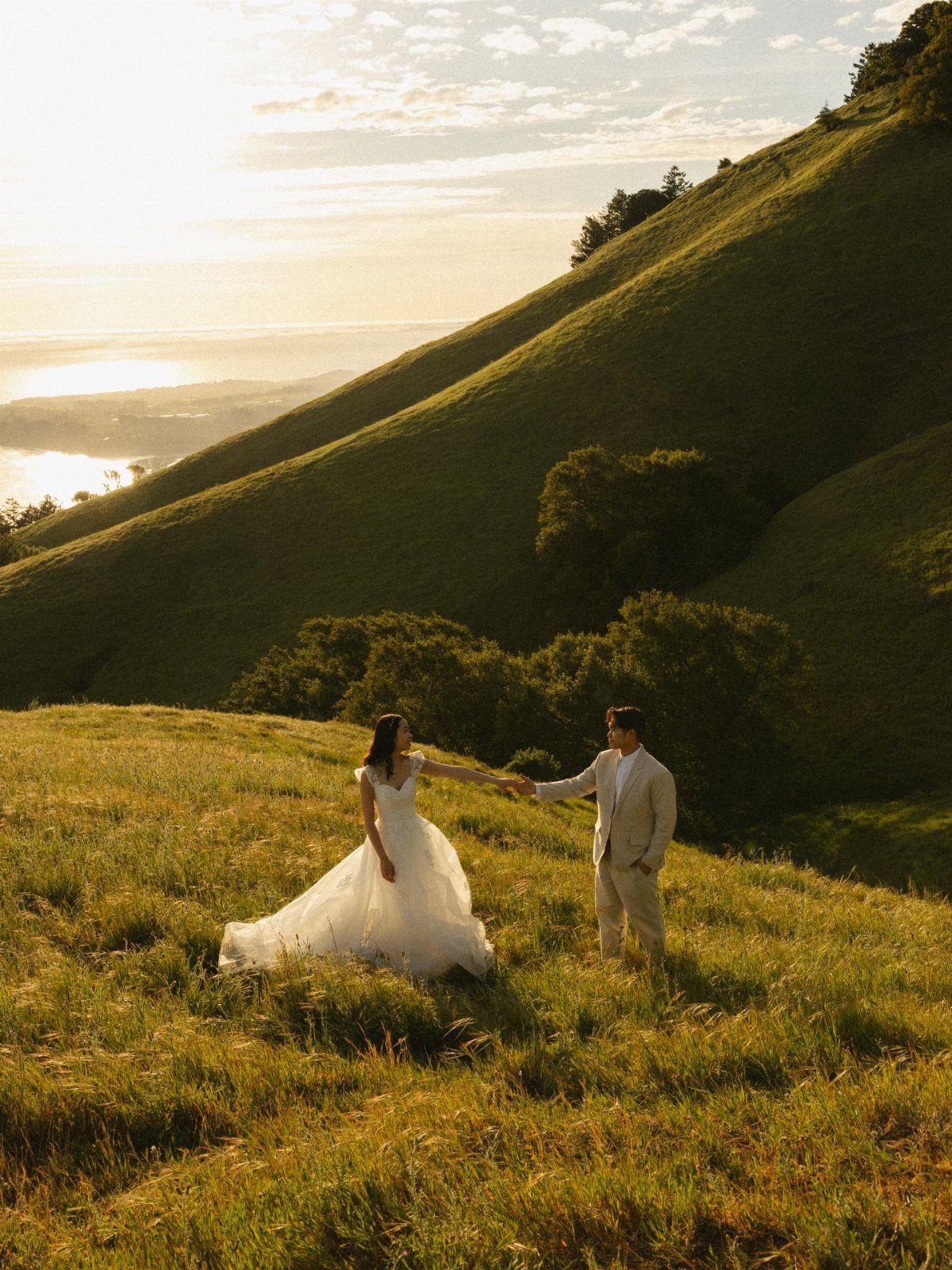 Couple in wedding attire holding hands in a grassy field with rolling hills.