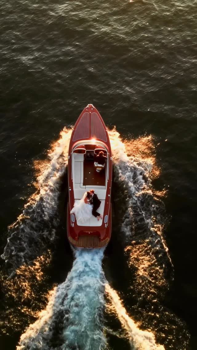 Couple in wedding attire embracing on a red motorboat speeding through dark water