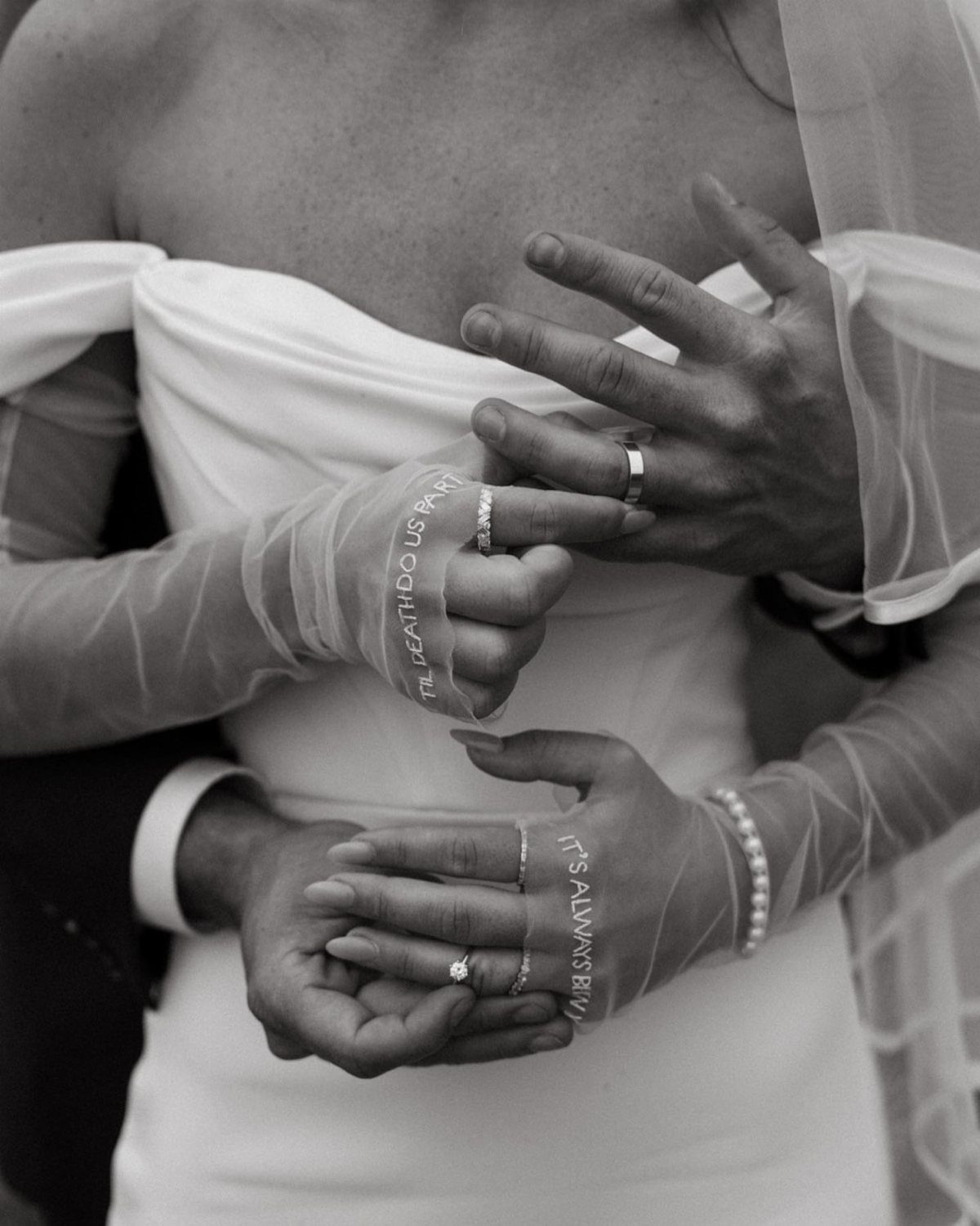 Bride in white dress showing wedding rings and sheer gloves with printed text.