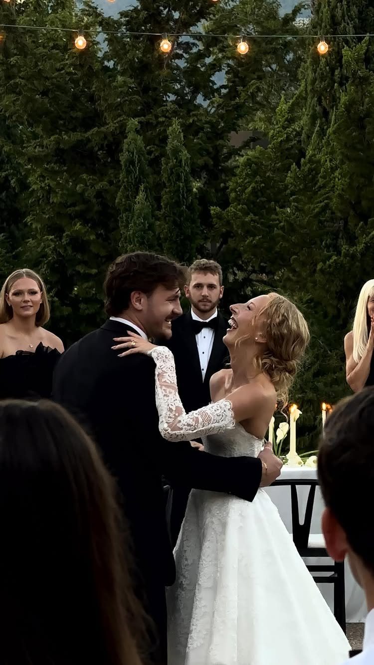 Bride and groom dancing outdoors at night under string lights with guests watching.